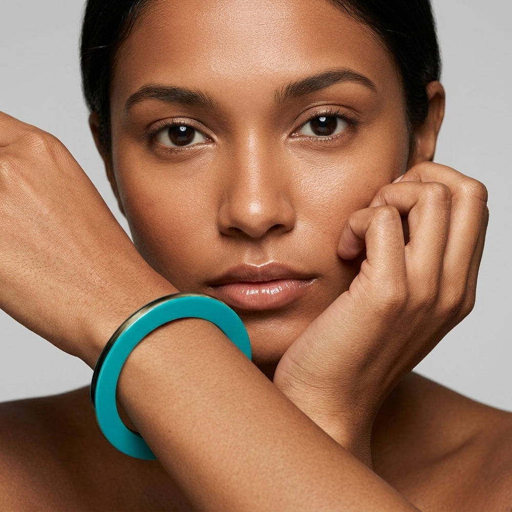 Woman wearing a Branch Jewellery Turquoise Blue lacquered natural horn flat bangle with Turquoise Blue lacquer on both sides and black natural horn rim, against  a neutral background