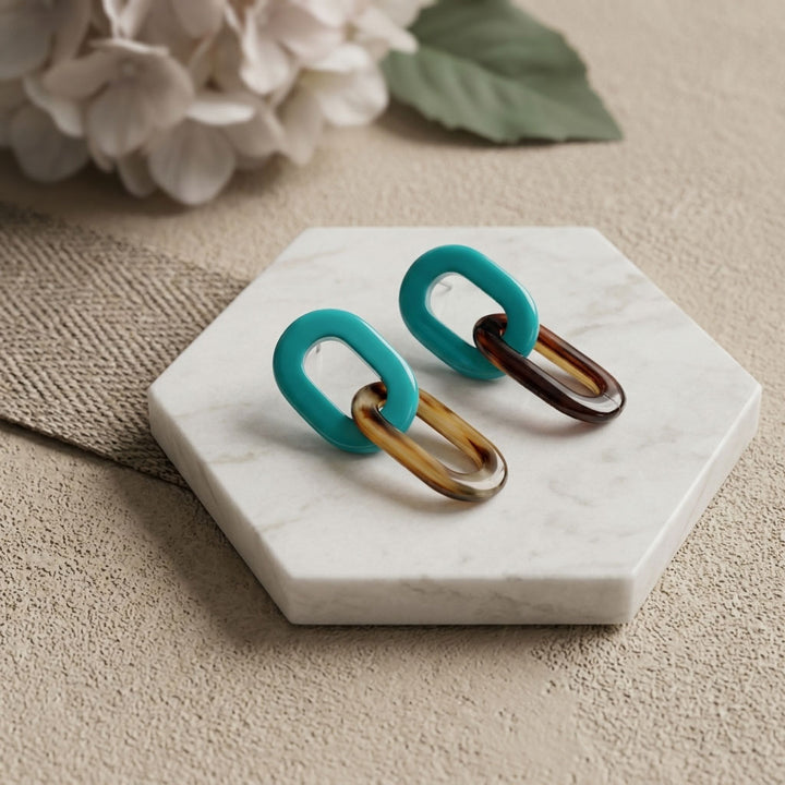 Pair of Branch Jewellery Turquoise Blue and natural black horn double oval link earrings on a marble stand with flowers in the background.