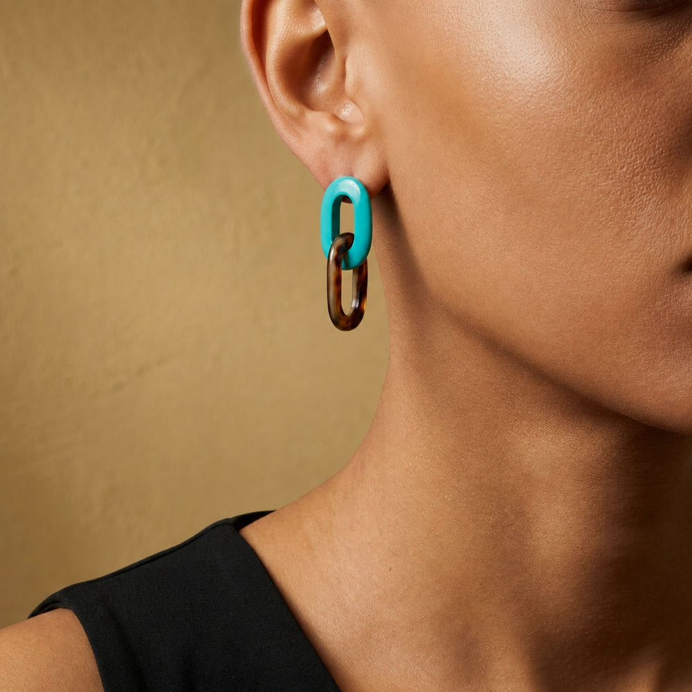 Close-up of an ear wearing a Branch Jewellery Turquoise Blue and natural black horn double oval link earrings  against a beige background