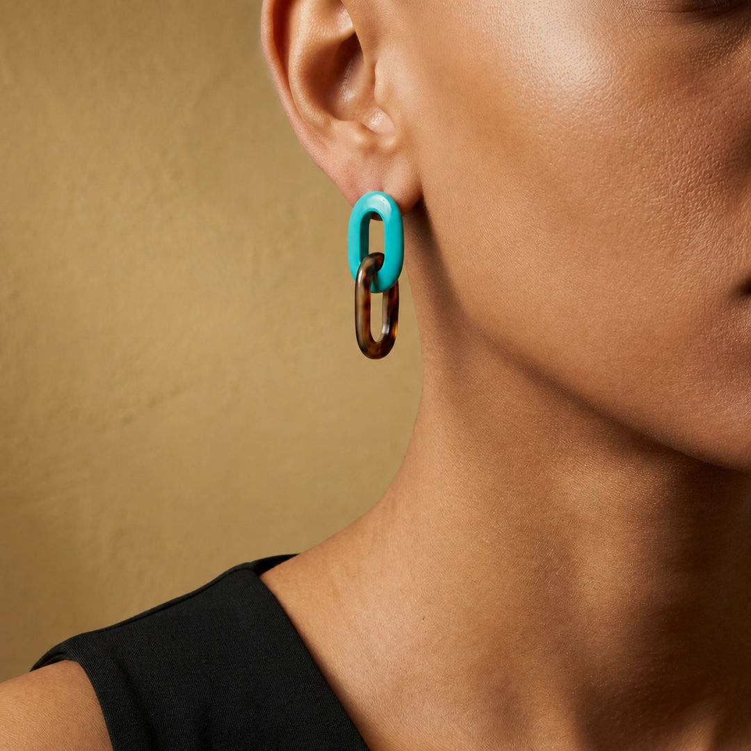 Close-up of an ear wearing a Branch Jewellery Turquoise Blue and natural black horn double oval link earrings  against a beige background