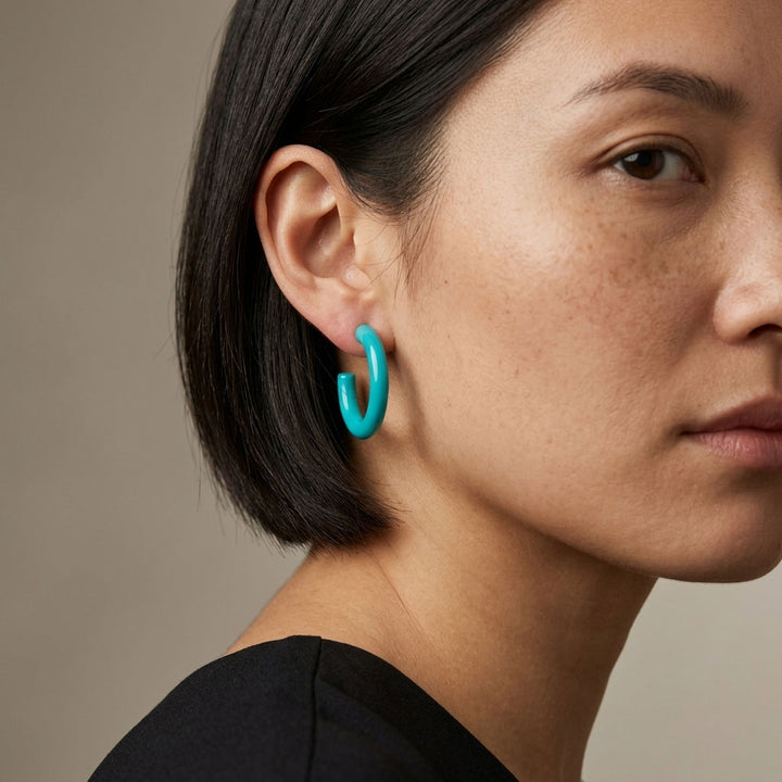 Close-up of a person wearing Branch Jewellery turquoise lacquered horn hoop earrings against a neutral background