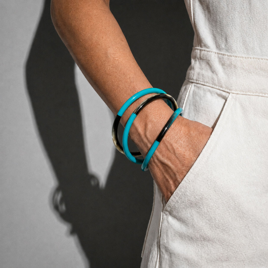 Person wearing Branch Jewellery set of three slim rounded bangles made from natural buffalo horn and Turquoise Blue lacquered horn.  Half of the bangle is black natural horn with natural markings and colourings, and the other half is covered with a smooth Turquoise Blue lacquer.
