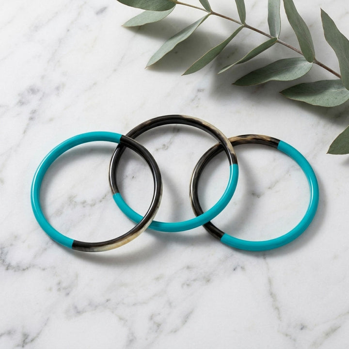Branch Jewellery Zuri Set of three Slim Turquoise Blue and Black Natural Horn Bangles on a marble surface with green leaves.