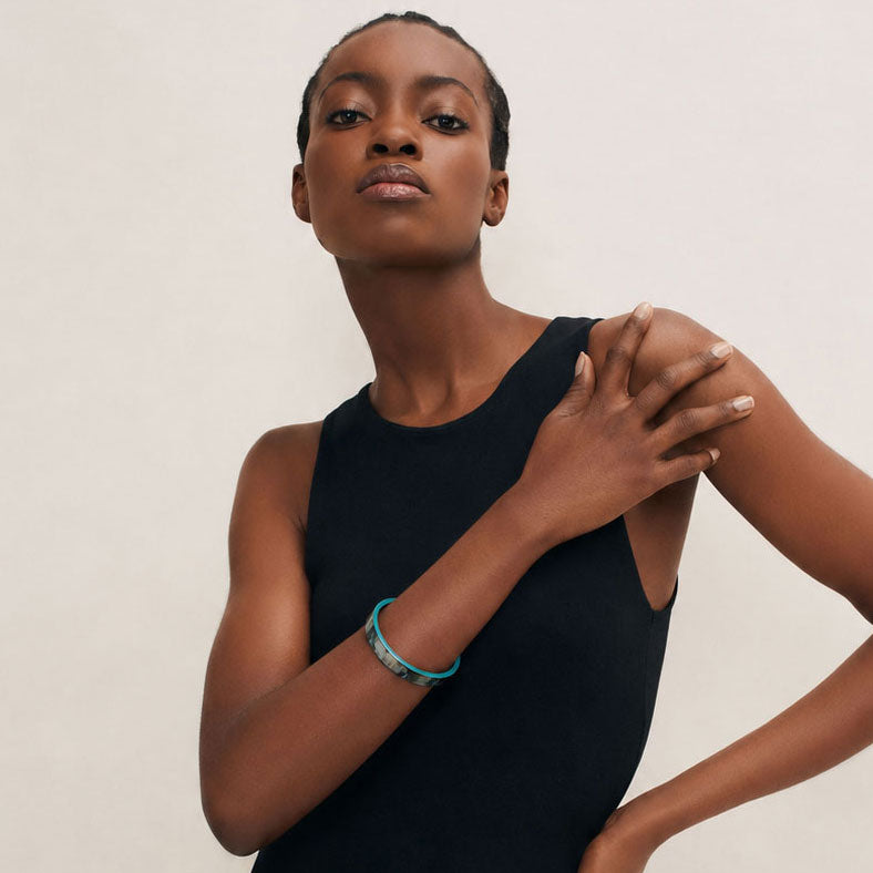 Woman wearing a Branch Jewellery Natural horn bangle with Turquoise Blue lacquered rim with black sleeveless top against a plain background