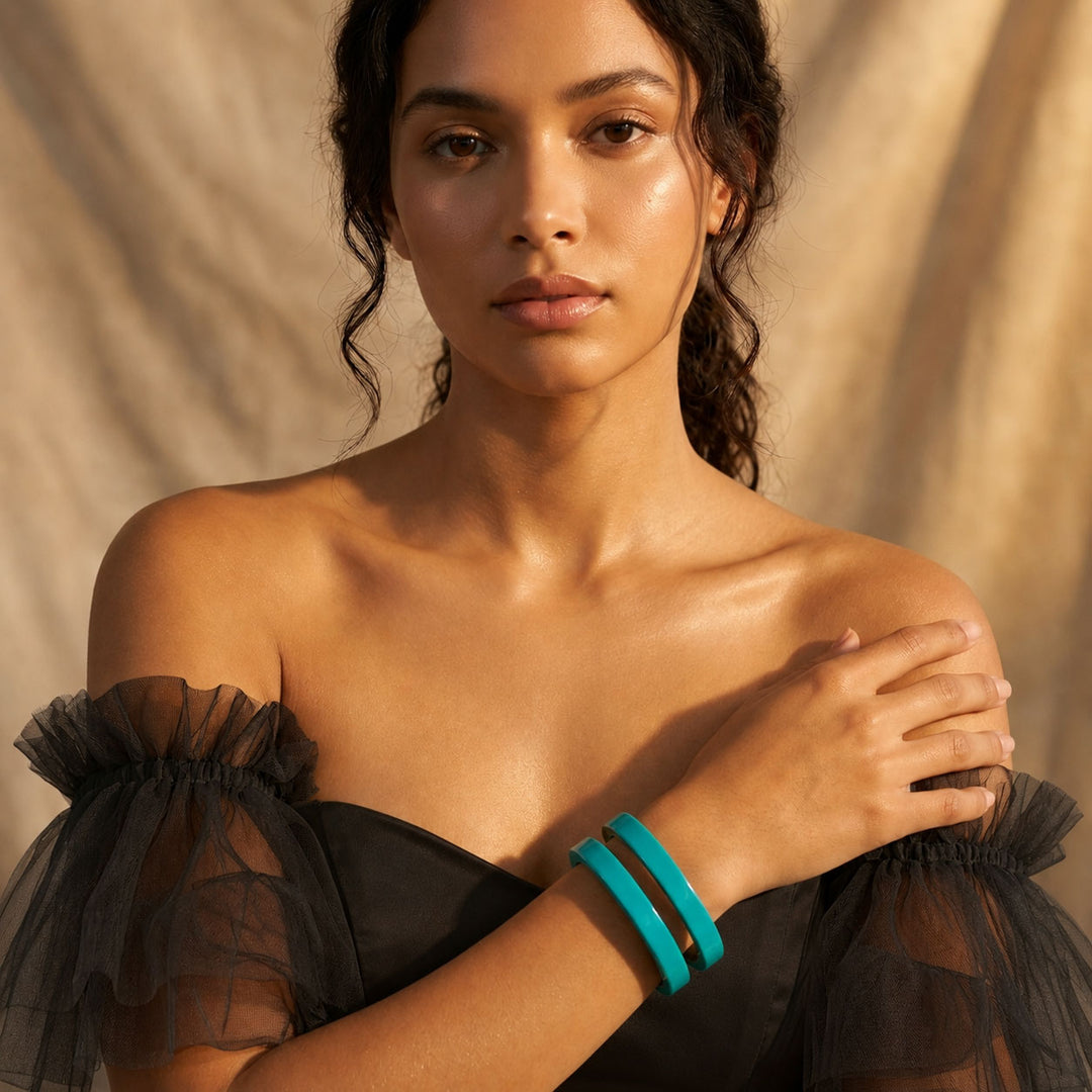 Woman wearing a Person wearing a Branch Jewellery Turquoise Blue cut-out cuff lacquered buffalo horn bangle cuff with a black off-shoulder top with sheer sleeves against a beige background