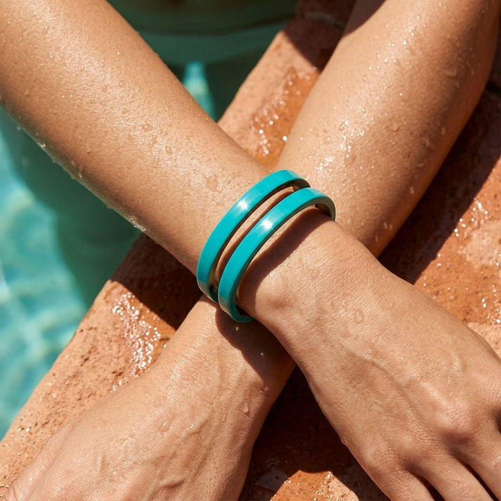 Close-up of a person's arm wearing a Branch Jewellery Turquoise Blue cut-out cuff lacquered buffalo horn bangle cuff on a neutral background by a poolside.