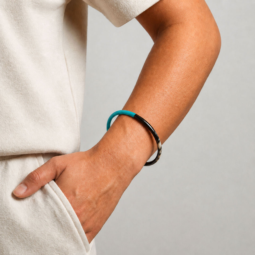 Person wearing a Branch Jewellery slim rounded black natural horn bangle with Turquoise Blue Lacquer. Half of the bangle is natural black horn and half is covered in a smooth Turquoise Blue lacquer.