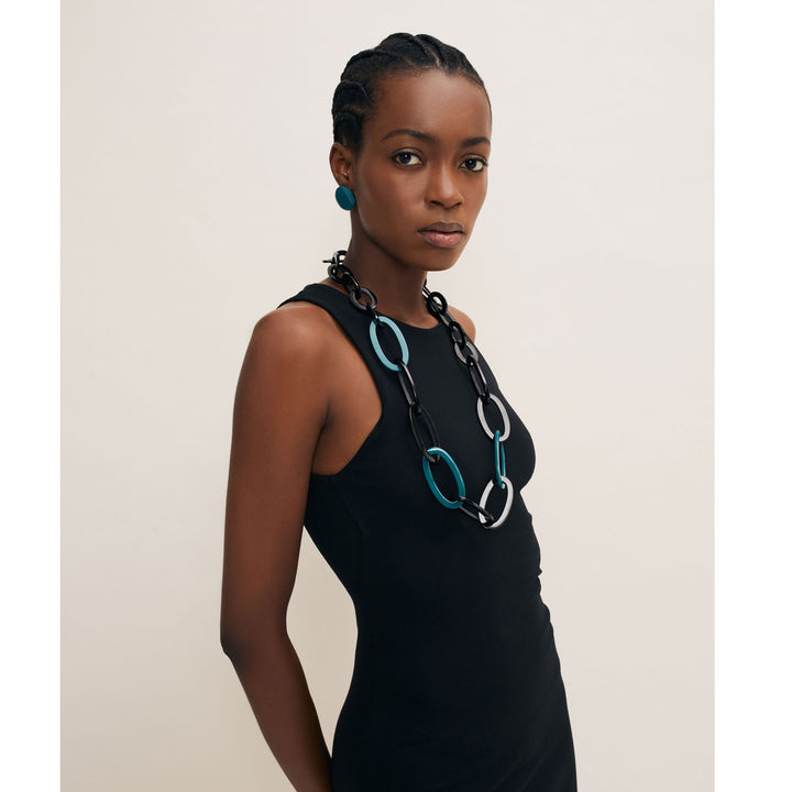 A person in a black sleeveless dress wears Branch Jewellerys Oval Link Black & Blue Horn Necklace and matching earrings. Styled in cornrows against a light background, the ethically sourced, handmade jewelry from Vietnam adds an elegant touch.